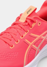 Asics running shoe in bright pink with orange accents, featuring a textured upper, flat laces, and a cushioned white sole.