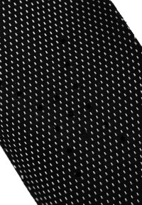 Black textured fabric featuring small, raised white triangular patterns and circular holes, creating a structured and patterned surface.