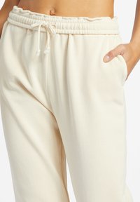 Sudaderas de color crema con una cinturilla elástica acanalada, cordón y bolsillos laterales, que presentan una textura suave y un ajuste casual.