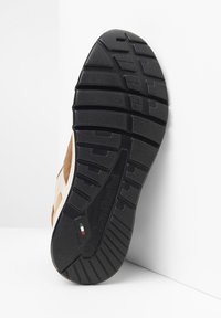 Suola di sneaker con fondo in gomma nera e modelli di trazione testurizzati, parte superiore in suede beige con una fascia in pelle chiara e dettagli con logo.