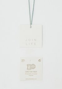 Deux étiquettes rectangulaires reliées par un cordon vert. L'étiquette du haut est blanche avec l'inscription « JOIN LIFE », celle du bas détaille les instructions d'entretien en texte doré.