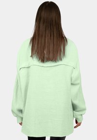 Camicia oversized verde menta in tessuto testurizzato, con design a spalle scese e orlo dritto.