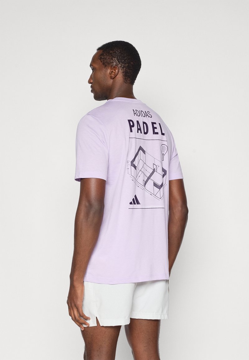 Jasnofioletowa bawełniana koszulka z krótkim rękawem z napisem "ADIDAS PADEL" oraz grafiką boiska do padla na plecach. Luźny krój, minimalistyczny design.