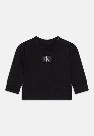 Camiseta negra de manga larga para niños pequeños, confeccionada en tela suave con cuello redondo, que presenta una etiqueta con un logo blanco en el frente y cierres de presión en el hombro.