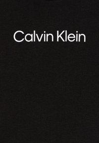 Juodas medvilninis marškinėliai su užrašu "Calvin Klein" ryškiu baltu sans-serif šriftu per krūtinę. Minkšta tekstūra, suapvalintu kaklu.