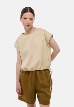 Top beige à manches courtes avec un col rond, une taille élastique et une coupe ample, associé à un short vert olive avec des poches latérales.