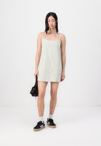 Vestido tipo tirantes en verde claro con rayas blancas verticales, con escote cuadrado y botones en el lateral, combinado con zapatillas negras.