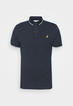 Marineblauwe polo met een klein wit stippenpatroon, korte mouwen, witte accenten op de kraag en manchetten, en een gele logo op de borst.