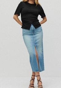 Haut noir à manches courtes avec détail froncé à la taille, associé à une jupe en denim bleu clair avec une fente à l'avant. Sandales noires à brides.