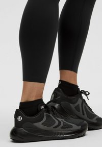 Scarpe sportive nere con una parte superiore testurizzata caratterizzata da un motivo a pois. Abbinato a leggings neri aderenti, che mostrano una silhouette elegante.