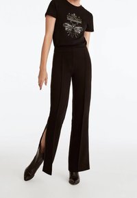 Sort T-shirt med sølv bi- og kronegrafik, parret med sorte flared bukser med sideslids og kontrasterende sømdetaljer.