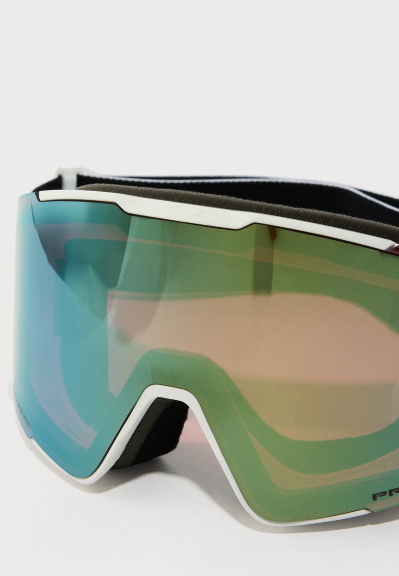 Skibril met een grote, groen-getinte lens met een gradient-effect, omringd door een witte rand en voorzien van een zachte zwarte band voor een veilige pasvorm.