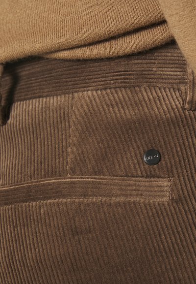 Brown corduroy fabric with vertical ribbing and a sleek black metal button. Features a back pocket with stitching detail.