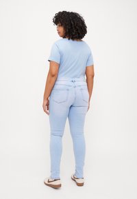Camiseta azul claro de manga corta, combinada con jeans skinny azul claro. El conjunto presenta un diseño ajustado y bolsillos traseros con forma curva.