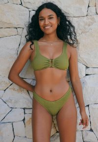 Olivgrünes, gestricktes Bikini-Set mit einem strukturierten Oberteil mit einem zentralen Schlüssel-Ausschnitt und breiten Trägern, kombiniert mit passenden, hochgeschnittenen Bottoms.