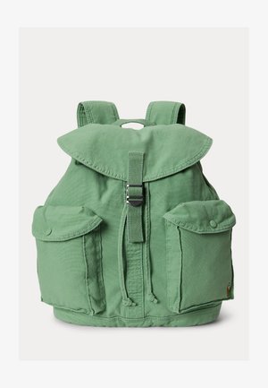 Zaļš auduma mugursoma ar pārsegu, centrālu sprādzes siksnu, aukliņām, divām priekšējām kabatām ar pogām un polsterētiem plecu siksnām.