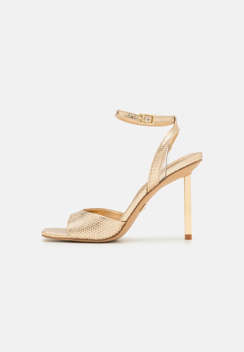 Kultaiset korkokenkä-sandaalit, joissa on teksturoitu metallinen viimeistely. Niissä on ohut nilkkahihna, avonainen kärki ja stiletto-korko.