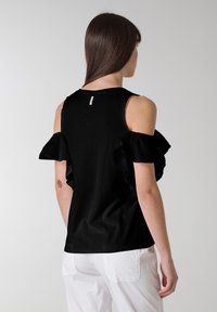 Sort t-shirt med cold-shoulder design og flæser ved ærmerne. Fremstillet af blødt stof, med et enkelt snit og en diskret label på ryggen.