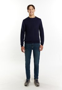 Maglione pullover blu navy con collo a giro, polsini e orlo a coste; abbinato a jeans blu e scarpe sportive grigio chiaro.