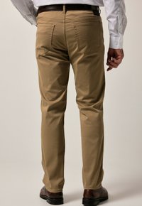 Beige chino's met een rechte pijp, zichtbare achterzakken en riemlussen. Het materiaal lijkt glad met een lichte glans.