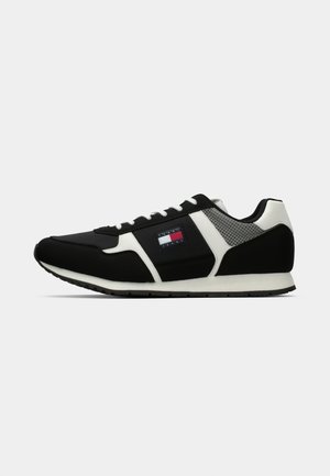 Black and white athletic sneakers with a mesh upper, textured panels, lace-up design, and a logo patch featuring red, white, and blue.