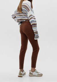 Bruine, slim-fit jeans met achterzakken, gecombineerd met een gestreepte trui in lichte tinten. De schoenen zijn meerkleurige sneakers.