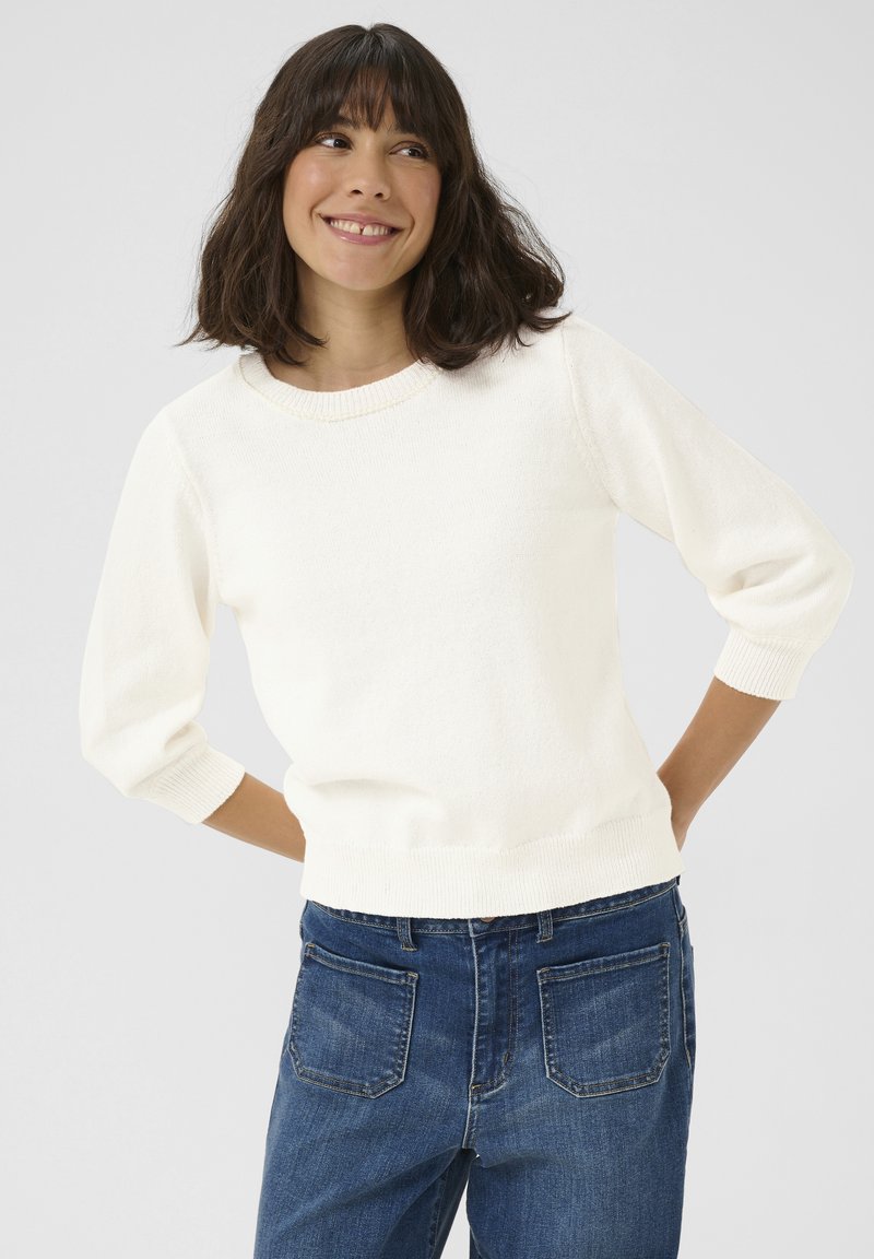 Pull-over crème avec un col rond et des manches 3/4, fabriqué en tissu tricoté doux, associé à un jean en denim bleu taille haute.