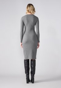 Robe midi rayée grise à manches longues, avec une silhouette ajustée. Portée avec des bottes noires en cuir montantes.