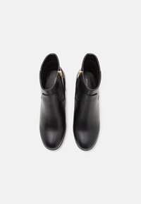 Bottines en cuir noir avec une texture lisse, un bout arrondi et des accents de fermeture éclair dorée sur les côtés. Design minimaliste, sans motifs visibles.