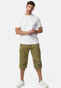 T-shirt en coton blanc associé à un short cargo vert olive. Les shorts ont des poches latérales et des manches retroussées, complétés par des baskets blanches.