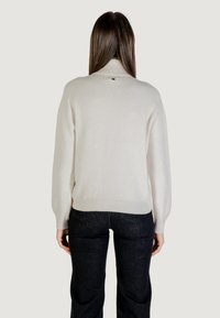 Pull en crème avec un col haut, des poignets et un ourlet côtelés. Présente des paillettes éparpillées sur un tricot lisse.