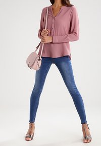 Chemise rose pâle à manches longues avec boutons, associée à un jean skinny bleu et des talons argentés à lanières. Petit sac bandoulière rose pâle.