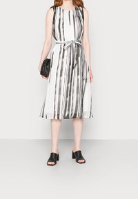 Ärmelloses Kleid mit schwarz-weißen vertikalen Streifen, tailliertem Bund, fließendem Rock und glattem Stoff. Kombiniert mit schwarzen, offenen Mules.