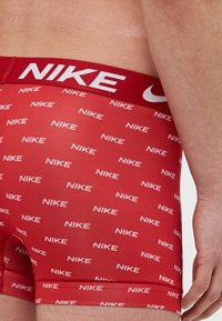 Czerwone bokserki z markowym elastycznym pasem. Tkanina zdobiona powtarzającym się białym wzorem logo "NIKE". Gładka faktura, dopasowany krój.