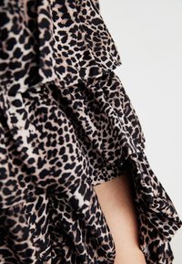 Leopardmønstret kjole med flæser, fremstillet i et blødt, let stof i nuancer af sort og beige. Fremhævede kantdetaljer.