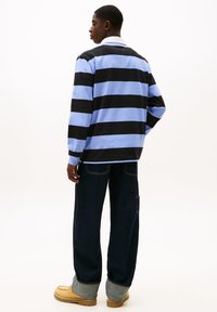 Maglia a maniche lunghe a righe in azzurro chiaro e nero, in misto cotone, abbinata a pantaloni in denim scuro e scarpe beige, che evidenziano un design casual e comfort.