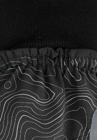Tessuto nero con una texture a coste nella parte superiore; la sezione inferiore presenta un polsino liscio ed elastico con un motivo a linee contornate bianche.