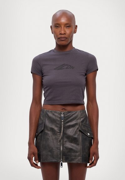 T-shirt gris crop avec un logo noir subtil, associée à une mini-jupe en cuir noir ajustée dotée d'une fermeture éclair sur le devant et de poches latérales.