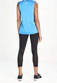 Niebieski bezrękawnik sportowy zestawiony z czarnymi legginsami z siateczkowymi panelami. Top ma okrągły dekolt; legginsy są dopasowane i 7/8.