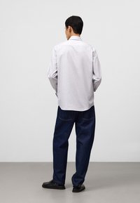 Vit långärmad skjorta med krage, kombinerad med lösa blå jeans. Skjortan har en slät yta; jeansen har synliga sömmar.