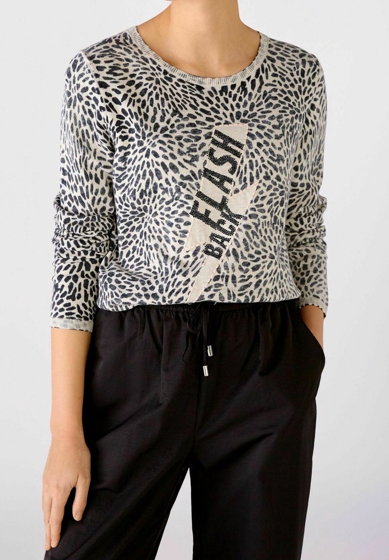 Personne portant un haut à manches longues imprimé animal avec un motif d'éclair et le texte « BACKFLASH », associé à un pantalon noir à cordon.