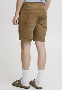 Pantaloni scurți bej din bumbac, cu tiv răsucit, două buzunare în spate și talie elastică. Purtați cu șosete albe și sandale maro.