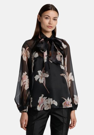 Black sheer blouse with large floral pattern in cream and pink hues, long sleeves, and a neck tie. Lightweight fabric with a soft texture.