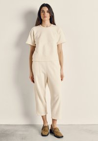Kremfarvet, tekstureret top med korte ærmer kombineret med matchende cropped bukser og brune træsko. Simpelt design med løs pasform.