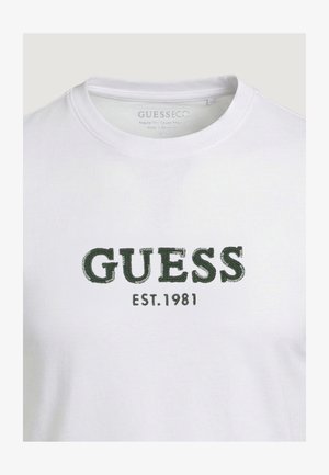 T-shirt blanc à col rond avec le texte "GUESS" vert brodé et "EST. 1981" en dessous sur la poitrine.