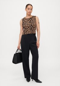 Top χωρίς μανίκια με animal print σε καφετί και μαύρο, σε συνδυασμό με ψηλόμεσα μαύρα παντελόνια, κρατώντας μία μαύρη τσάντα. Μαύρα παπούτσια ολοκληρώνουν την εμφάνιση.