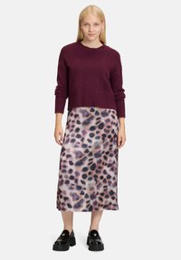 Bordeaux cropped trui met afgewerkte onderkant, gecombineerd met een lange rok met een gelaagde, abstracte luipaardenprint in roze en zwarte tinten.