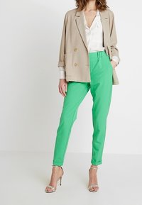 Groene op maat gemaakte broek met een gladde textuur, voorzien van zijzakken en een slim fit. Gecombineerd met een lichtbeige dubbel-gebreid colbert.