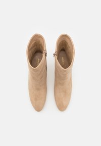 Bottines beige en daim, avec un bout arrondi et une fermeture éclair latérale. Texture lisse avec un design minimaliste.