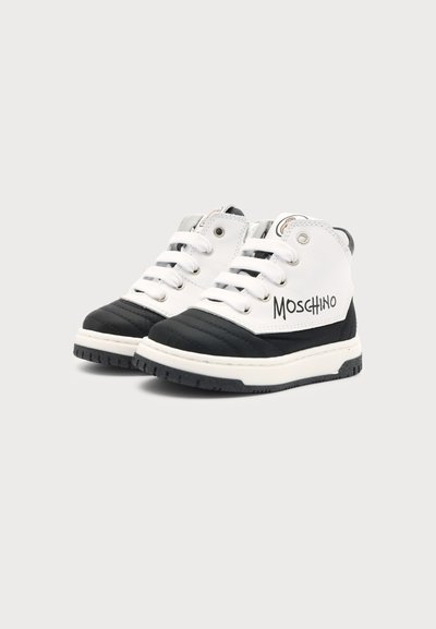 Ζευγάρι ασπρόμαυρα ψηλά sneakers Moschino με λευκά κορδόνια και χοντρές λαστιχένιες σόλες σε ανοιχτό φόντο.